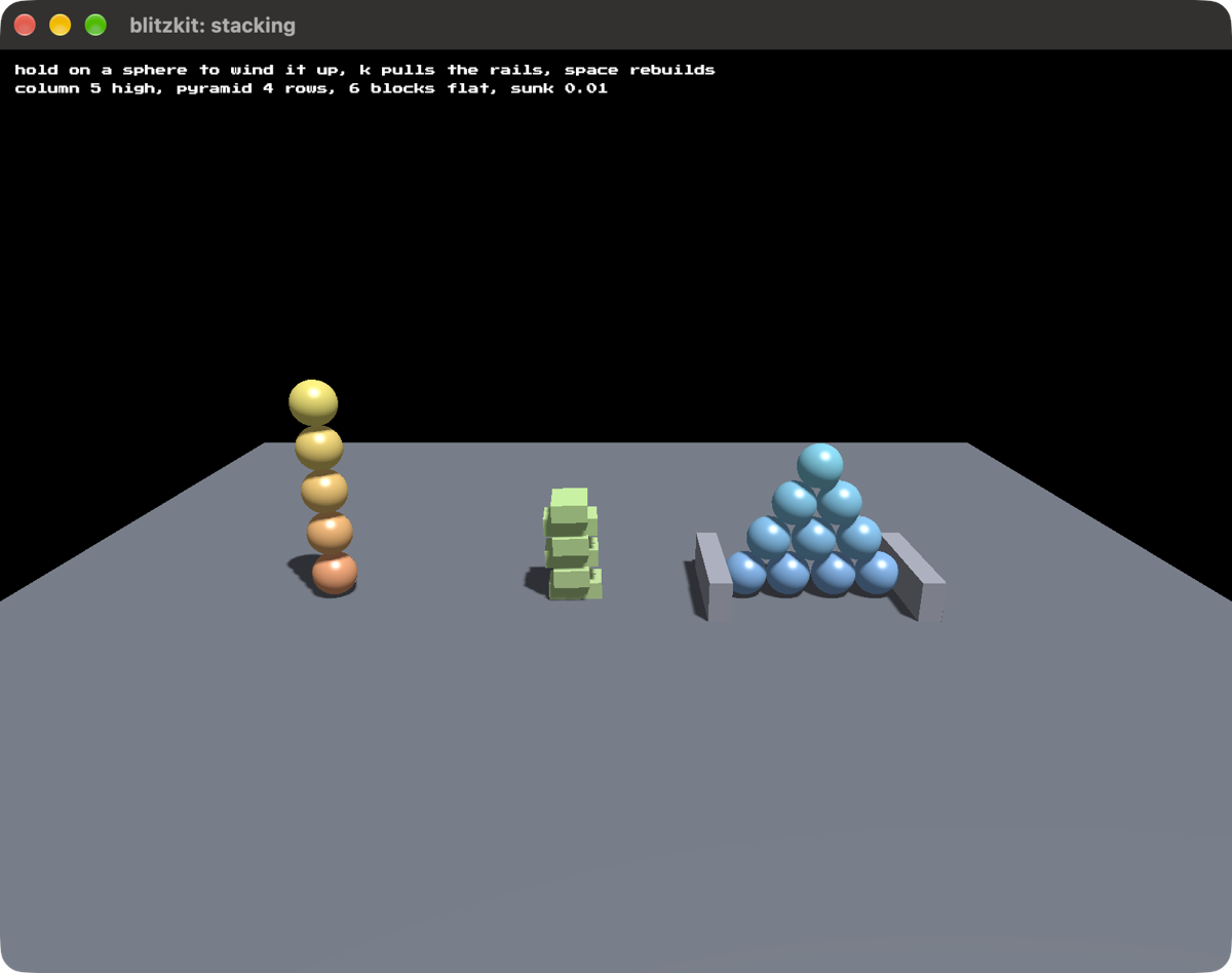 A column of five spheres, a heap of green blocks, and a pyramid of ten
spheres between two low rails, standing on a grey floor